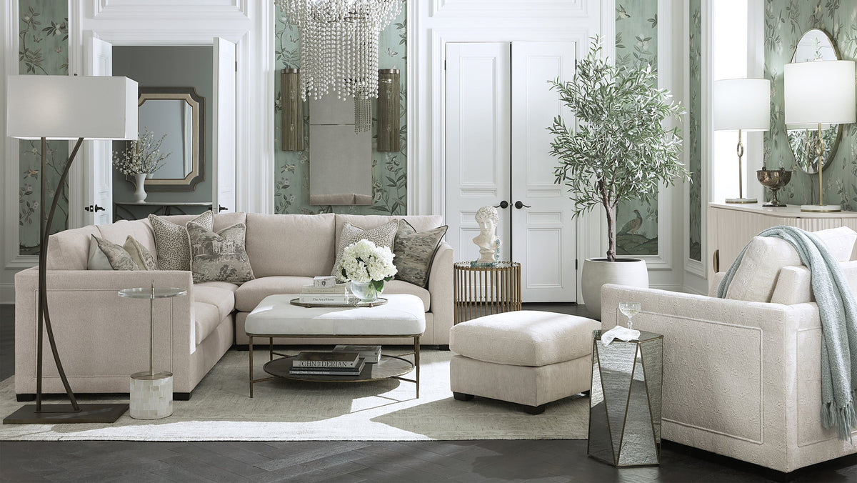 Gabby indoor upholstered sectional sofa and ottoman in soft neutral fabric styled in a transitional living room at Gabriella White, with mirrored doors, a chandelier, and elegant layered furnishings throughout.